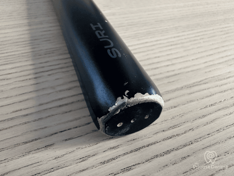 Close-up-of-the-base-of-a-black-SURI-electric-toothbrush-showing-chips-and-wear-on-the-aluminum-finish-after-long-term-use