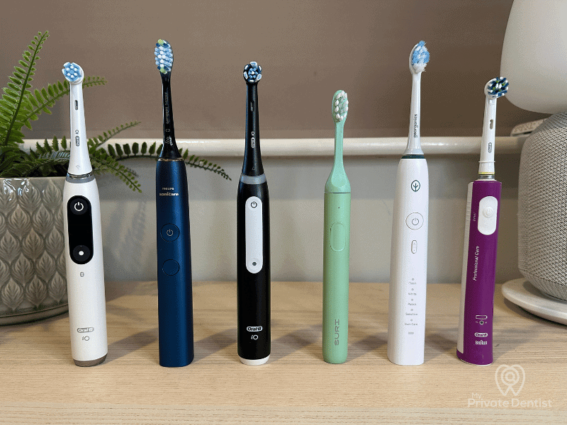 A lineup of the best electric toothbrushes for 2025 reviewed by My Private Dentist, featuring models from Oral-B iO, Philips Sonicare, and SURI arranged side-by-side on a desk.