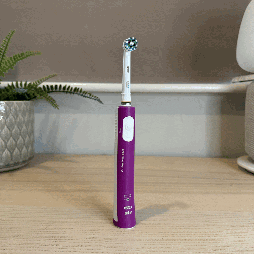 Purple Oral-B Pro Kids electric toothbrush, designed for children, standing on a desk.