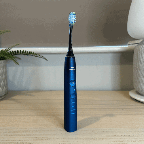 Philips Sonicare 9000 electric toothbrush in a dark blue finish, standing on a desk.