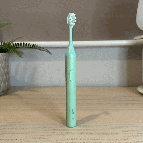 Suri 2.0 sustainable electric toothbrush in mint green, standing upright on a wooden desk.